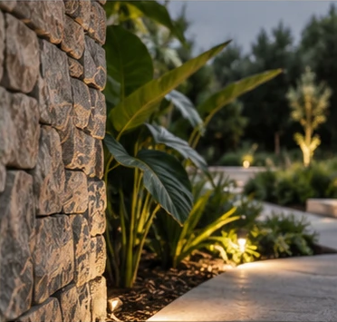 A stone wall and lush planting beside a lit garden path
